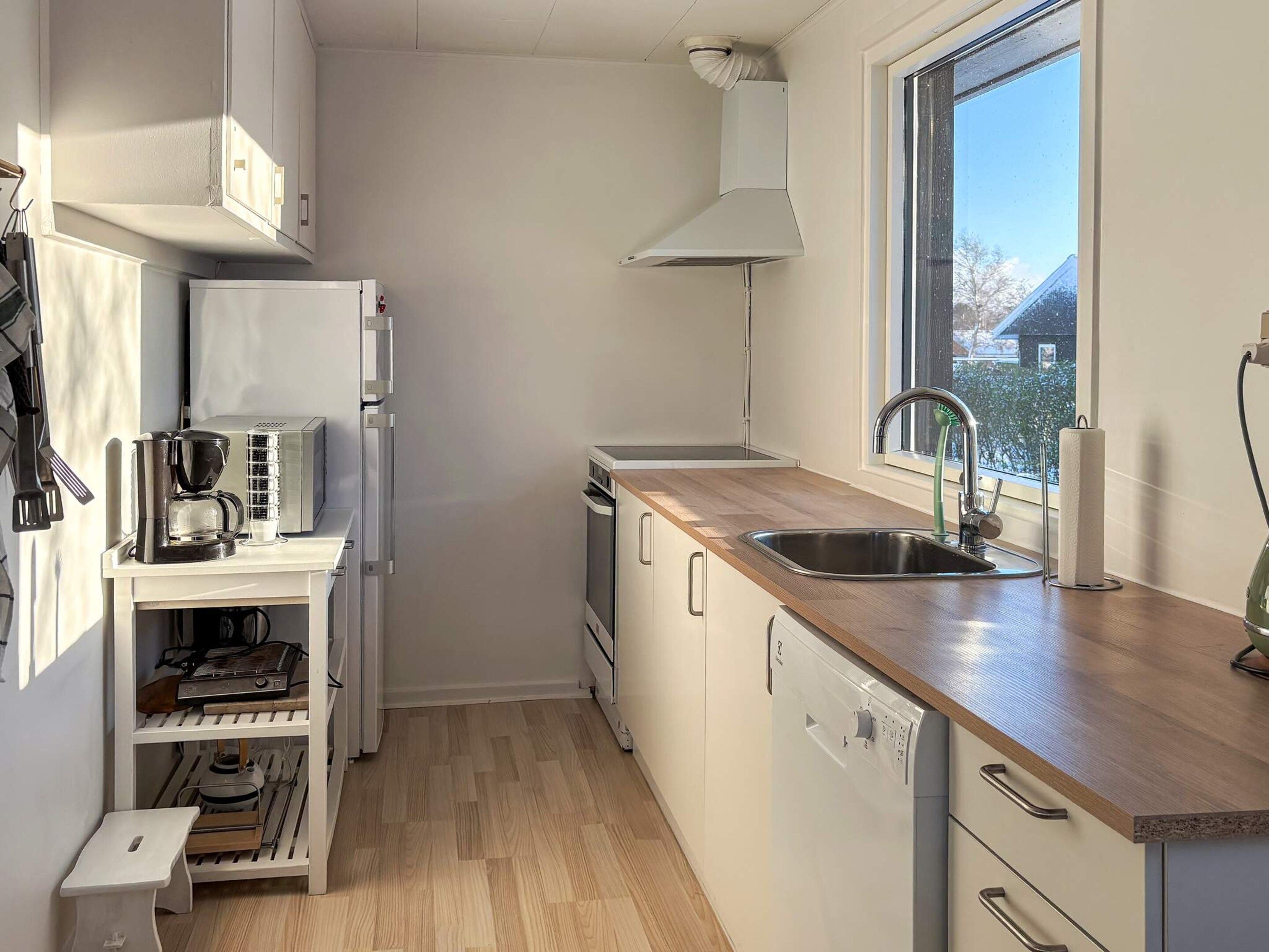 A compact kitchen with a built-in dishwasher, a coffee maker, and a window providing a view of the outside.