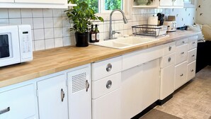 Une cuisine moderne avec des meubles blancs, un plan de travail en bois, un four à micro-ondes, un évier et une fenêtre donnant sur un espace verdoyant.