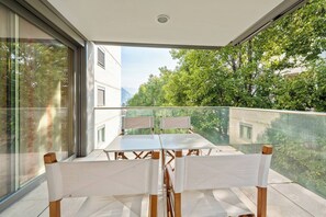 A balcony with a table and chairs, large windows, and a view of trees and buildings. - Luxury Apartment The DOM Lugano (Lugano)