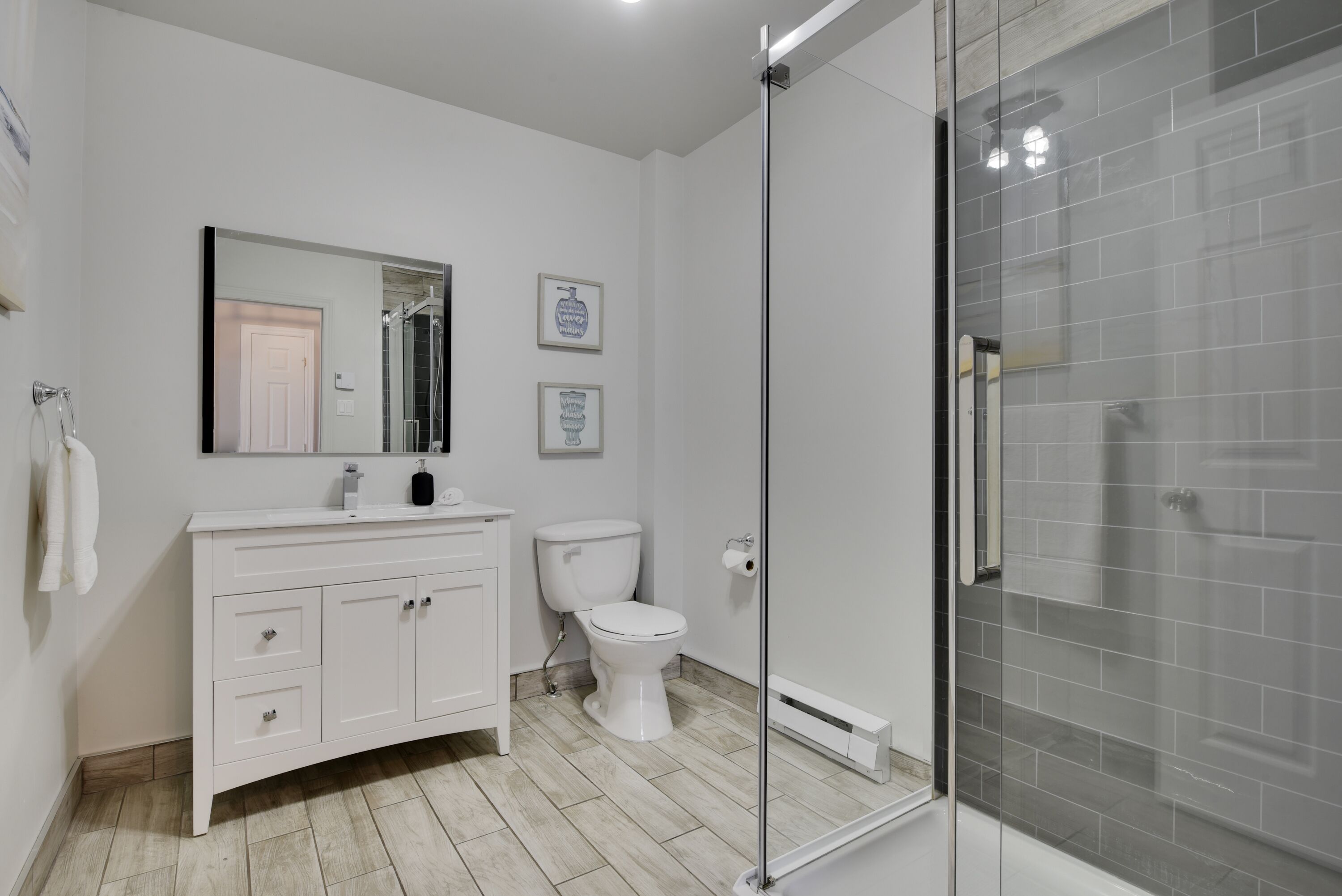 A modern bathroom with a white vanity, toilet, and a glass-enclosed shower area.