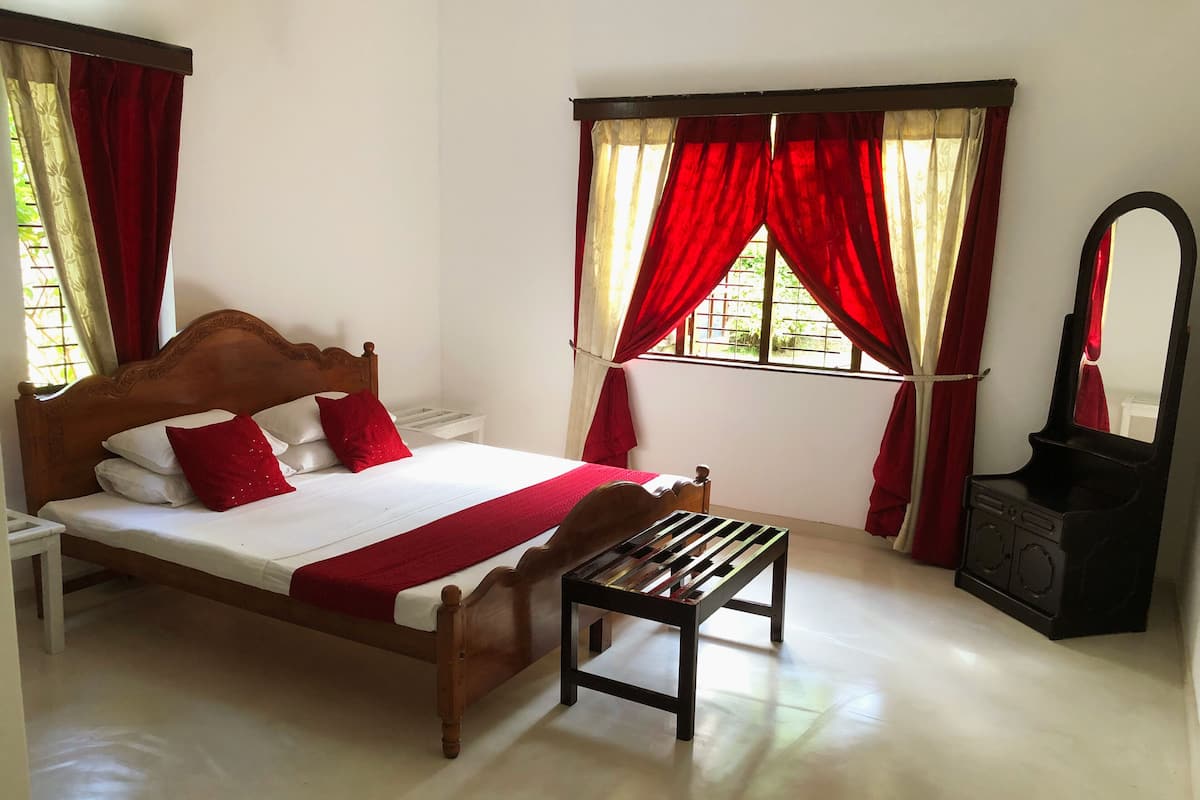 A bedroom with a wooden bed, red and white bedding, a small table, and a stove.