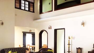 Um quarto espaçoso com uma grande mesa de jantar de madeira, várias cadeiras, um sofá e um ventilador de teto.