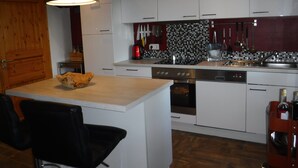 Eine moderne Küche mit weißen Schränken, einer zentralen Kochinsel, einer schwarzen Pendelleuchte und einem Weinkühlschrank.
