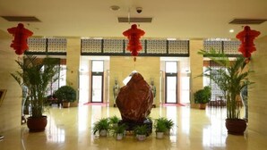 A spacious lobby with a large central rock sculpture, potted plants, and red decorative elements. - Spring Hotel (Dacheng)