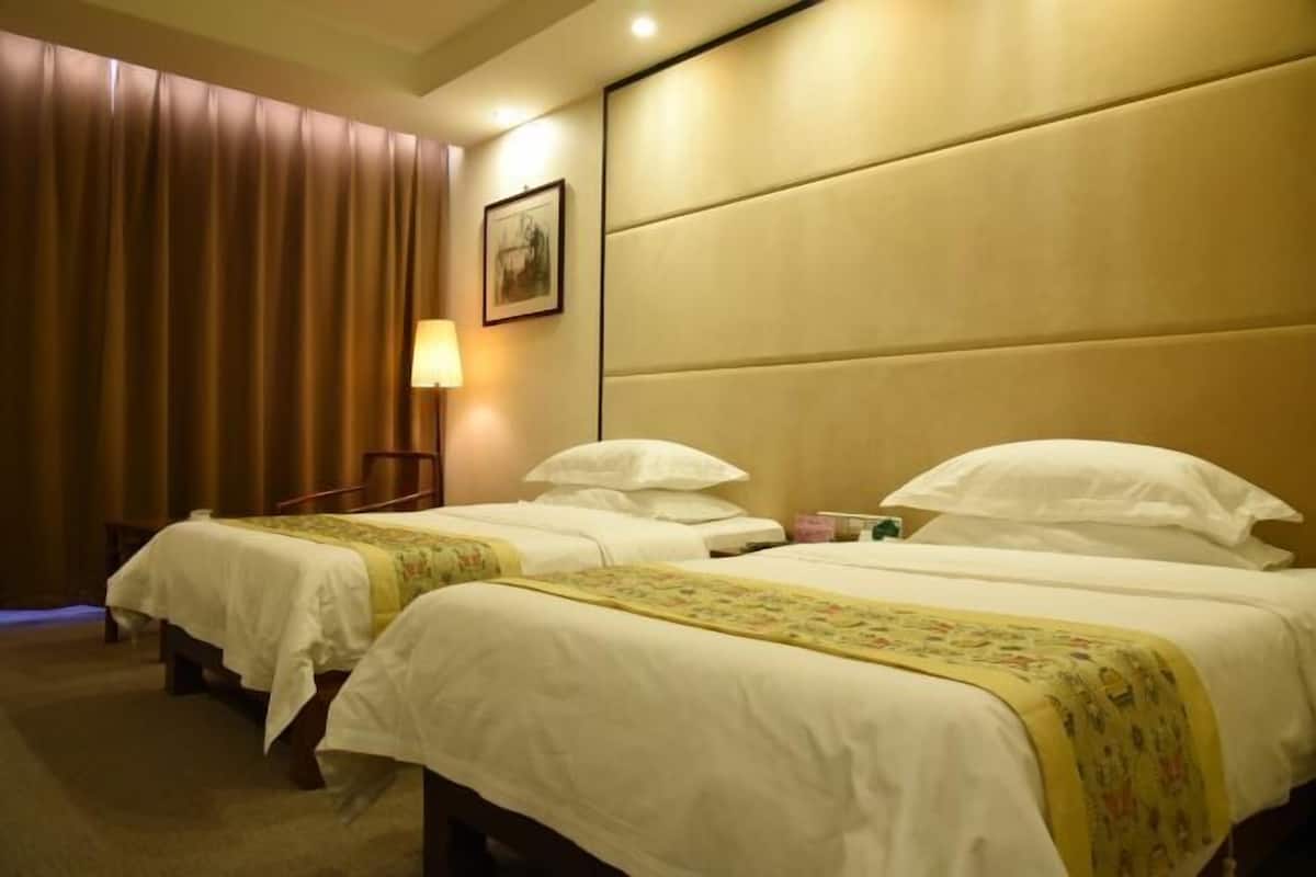 A hotel room with two beds, a wall-mounted TV, a bedside table, and a lamp.