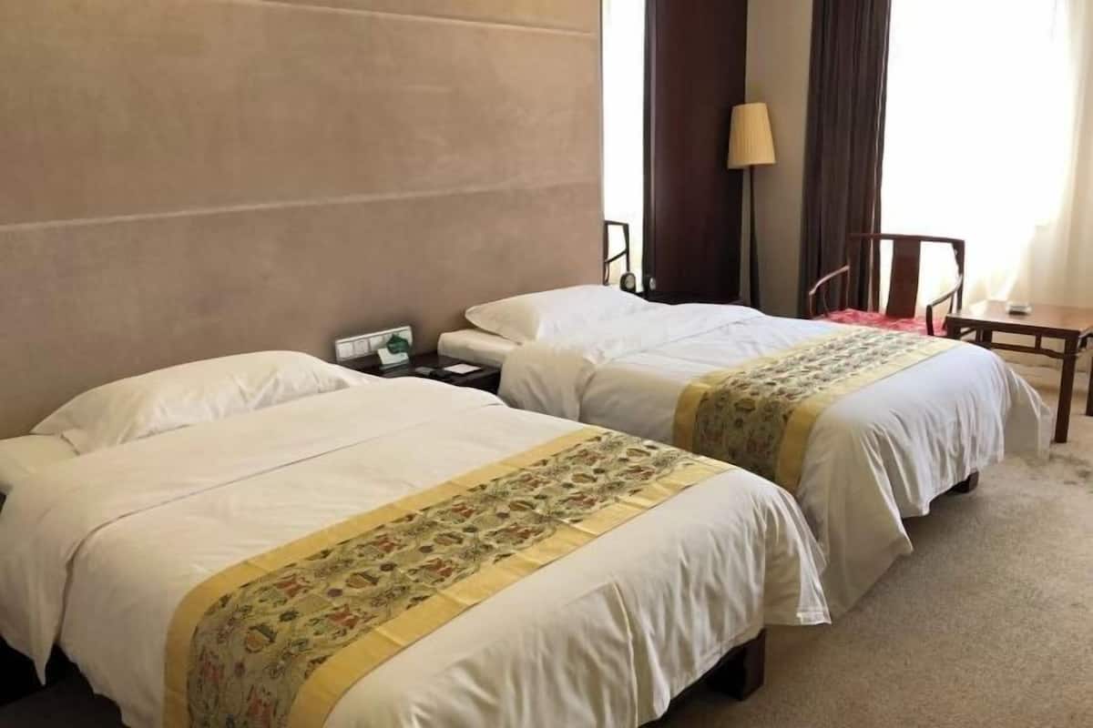 A hotel room with two beds, a nightstand, a lamp, a chair, and a small table.