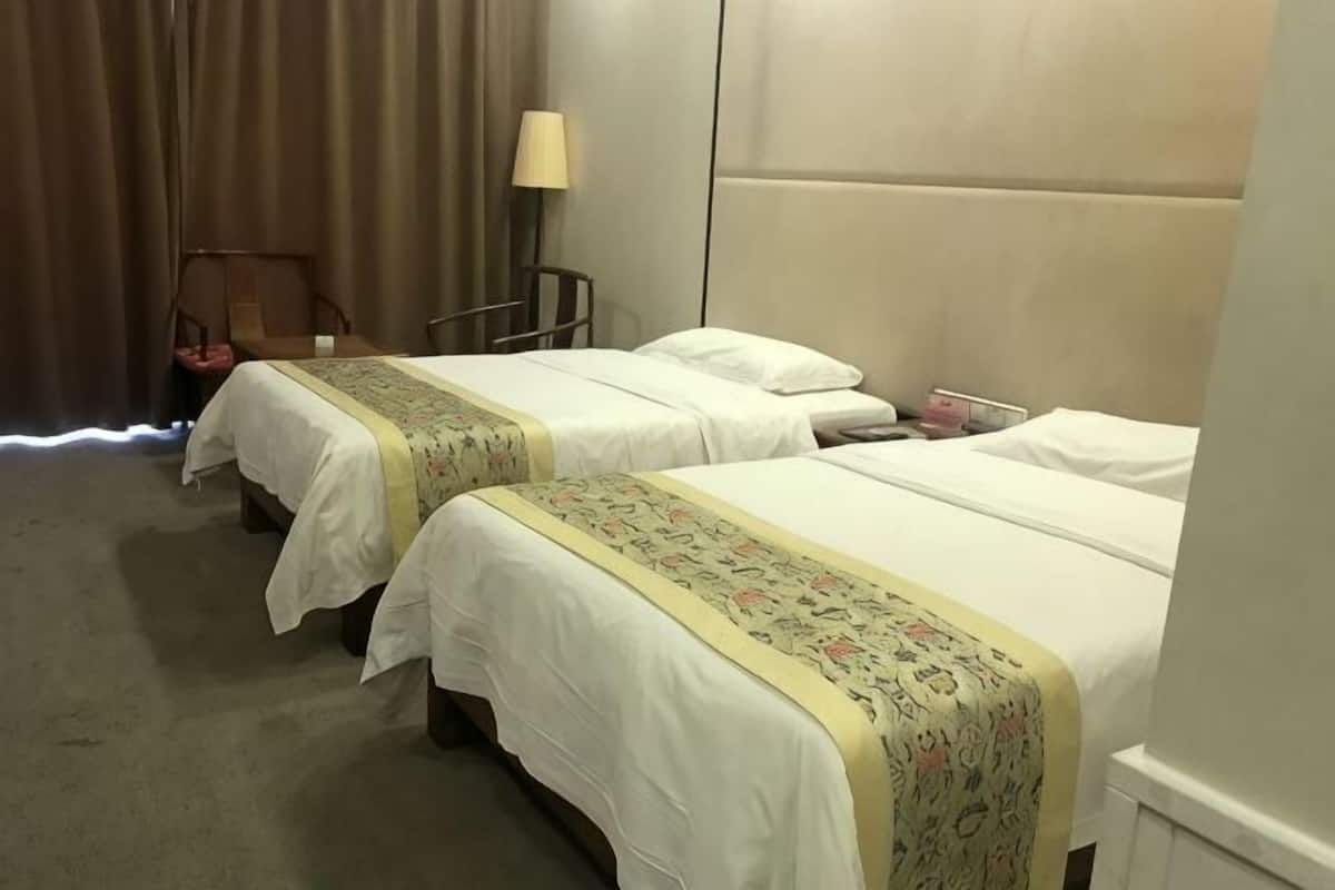 A hotel room with two beds, a chair, a lamp, and a curtain.
