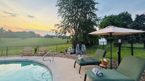 A pool area with lounge chairs and an umbrella, surrounded by a fence and trees. - Luxury Home w/private Pool, Mt Views, 85” Roku Movie Room, Arcade, & King Bed! (Talbott)