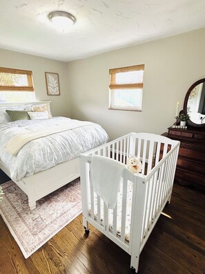 Une chambre à coucher avec un lit, un berceau, une commode et une fenêtre donnant sur un beau paysage.