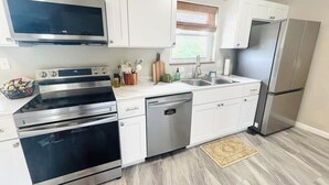 A modern kitchen with white cabinets, stainless steel appliances, and a window with blinds. - Luxury Home w/private Pool, Mt Views, 85” Roku Movie Room, Arcade, & King Bed! (Talbott)