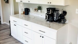 A kitchen with white cabinets, a marble countertop, and a coffee maker. - Luxury Home w/private Pool, Mt Views, 85” Roku Movie Room, Arcade, & King Bed! (Talbott)