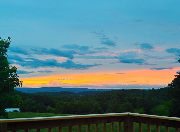 Une terrasse en bois donnant sur un paysage boisé, avec un ciel au coucher du soleil.