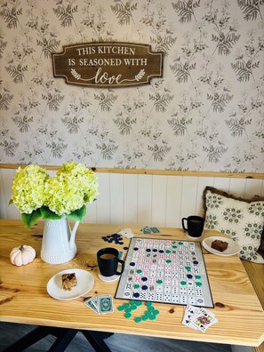 Une table en bois avec un jeu d’échecs, des cartes, une tasse, un vase de fleurs et un panneau accroché au mur.