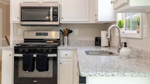 Une cuisine avec des armoires blanches, une cuisinière en acier inoxydable, un four à micro-ondes et un comptoir en granit.