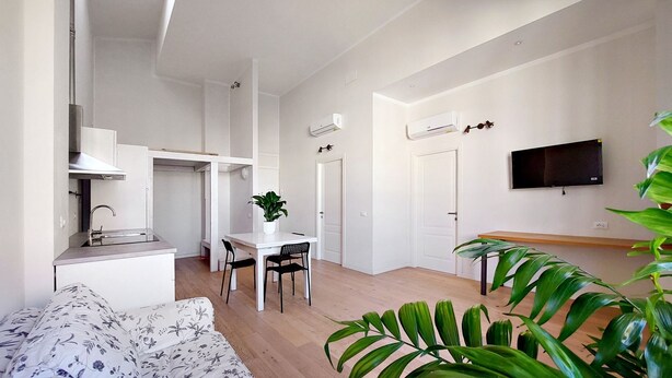 Een compacte woonruimte met een kitchenette, een eethoek en een aan de muur bevestigde televisie.