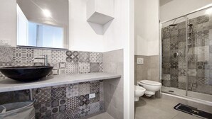 Een moderne badkamer met een grote zwarte wastafel, een douche met glazen wanden en een toilet.