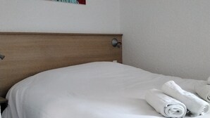 A neatly made bed with white linens and rolled towels, a wooden headboard, and a painting of red flowers on the wall. - Comfortable Apartment for Six in Alsace (Saales)