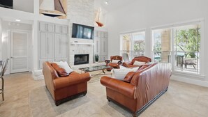 A spacious living room with leather sofas, a fireplace, and large windows offering a view of the outdoors.