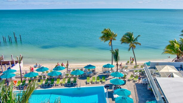 A poolside area with lounge chairs and umbrellas, a clear view of the ocean, and a sandy beach. - Cabana Club, Kayaks, Pets, Boat Dock, Near Golf! (Key Colony Beach)