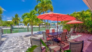 A patio area with a table and chairs, surrounded by palm trees and a view of a marina. - Cabana Club, Kayaks, Pets, Boat Dock, Near Golf! (Key Colony Beach)