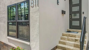 A building with a large window, a door with a glass panel, and a small outdoor area with steps and a railing.