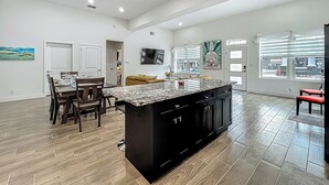 A spacious kitchen with a large island, wooden flooring, and a dining area with chairs and a table.
