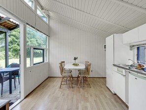 A room with a dining table, chairs, a kitchen area with a sink, and large windows allowing natural light. - 4 Person Holiday Home in Hampen (Hampen)