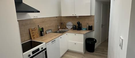 A compact kitchen with white cabinets, a black range hood, and a wooden countertop.