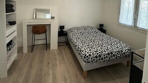 Ein Schlafzimmer mit Bett, Schreibtisch, Stuhl, Kleiderschrank und Fenster.
