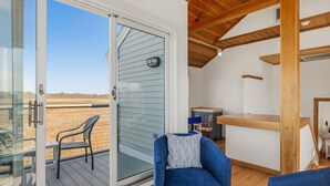 Una habitación con puerta corrediza de vidrio que da a un balcón, un sofá azul, una mesita y una estructura de techo de madera.