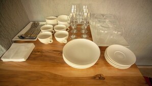 A wooden table with white plates, bowls, cups, wine glasses, and a set of cutlery. - Pollux (Batumi)