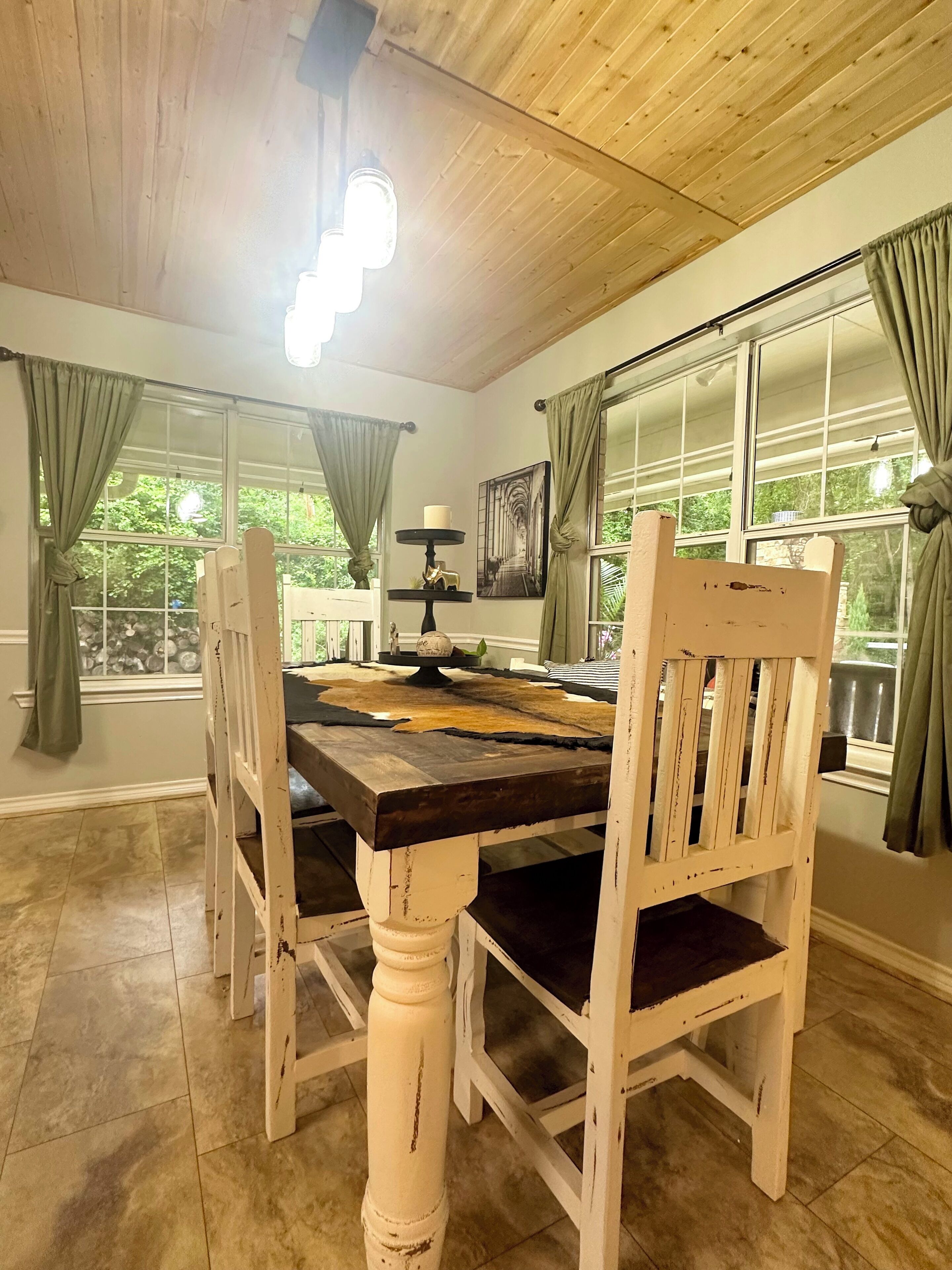 Un coin repas avec une table et des chaises en bois, un lustre et de grandes fenêtres ornées de rideaux.