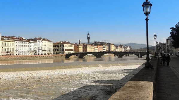 A river with a stone bridge, buildings along the riverbank, and a lamppost on the sidewalk.