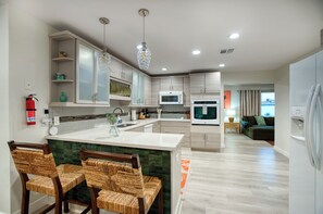 A modern kitchen with a central island, built-in appliances, and a dining area with wicker chairs. - A tropical Scottsdale escape made for friends and family to gather, relax and reconnect. Enjoy your private pool, tiki bar and inviting spaces to spend time together—all just a 10-minute drive from Old Town (Scottsdale)