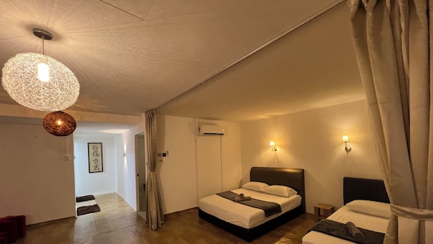 A hotel room with two beds, a wooden floor, a hanging light fixture, and a wall-mounted air conditioner. - COMFORTABLE STAY HOME (Ayer Itam)