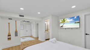 Un dormitorio con cama, televisor y un cuadro de una playa.