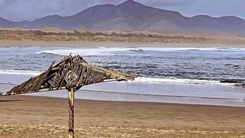 Una platja amb una estructura de fusta, possiblement un banc o un senyal, i una serralada de muntanyes al fons.