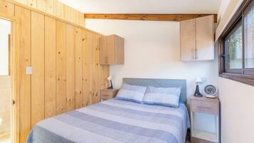 A bedroom with a bed, wooden wardrobe, bedside table with lamp, and a window.