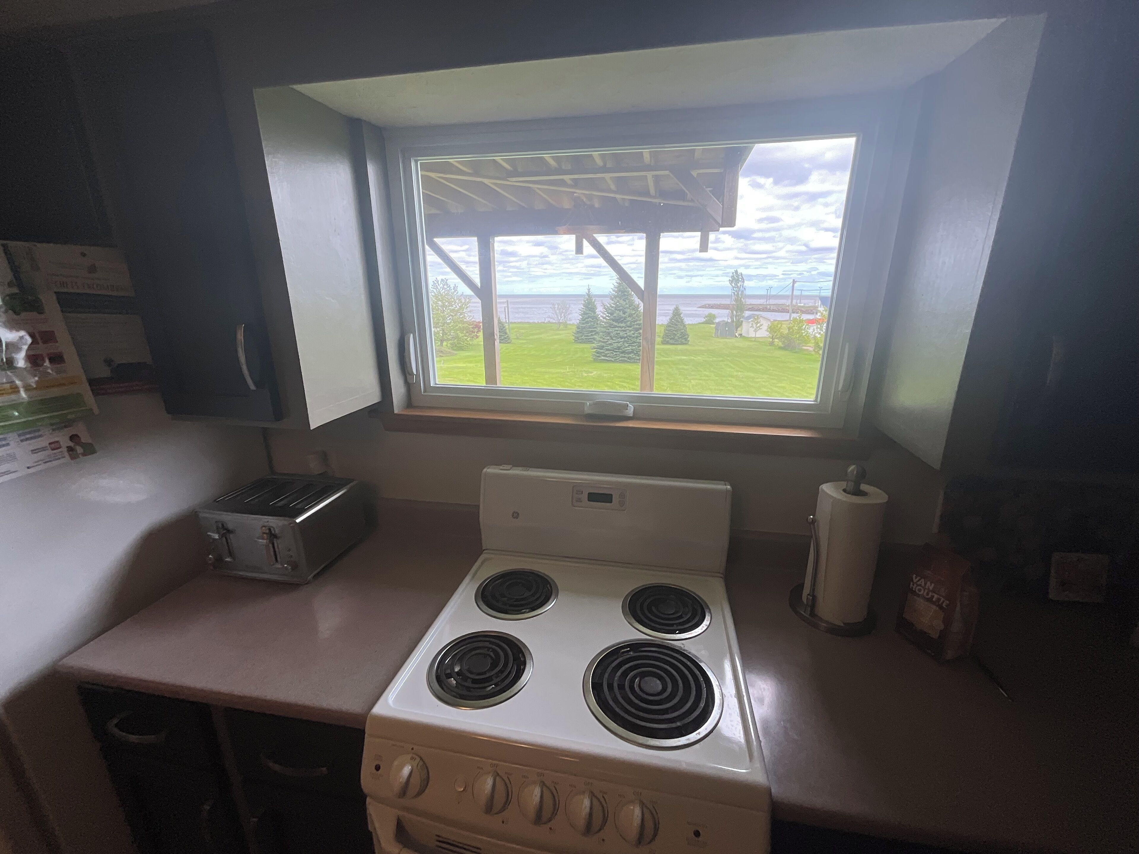 Una cucina con un fornello, una finestra vista esterna e un cestino.