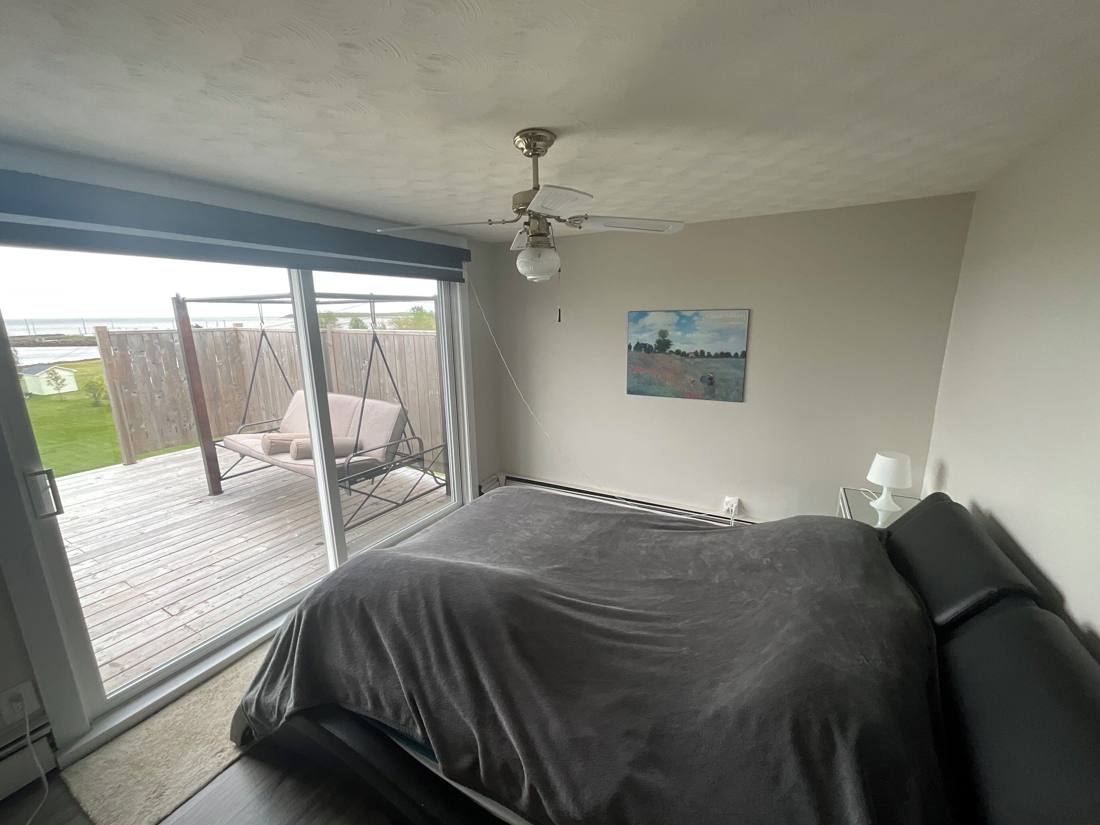 A bedroom with a bed, a ceiling fan, a window, and a view of a deck and outdoor area.