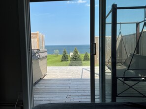 An open door leading to a balcony with a view of the sea, a wooden deck, and a swing chair. - Oceanfront paradise, 4-bedroom house in Cocagne with hot tub, WiFi, AC. (Cocagne)