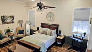 A bedroom with a bed, a nightstand, a desk, a chair, a lamp, and a ceiling fan. - Scenic Serene Spacious Studio 65in Smart TV WiFi Sun Ticket Laundry Full Kitchen (Decatur)
