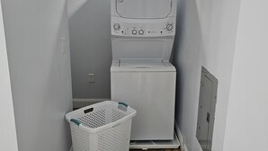 Uma lavanderia com máquina de lavar e secadora empilhadas, um cesto de roupa e piso cerâmico.