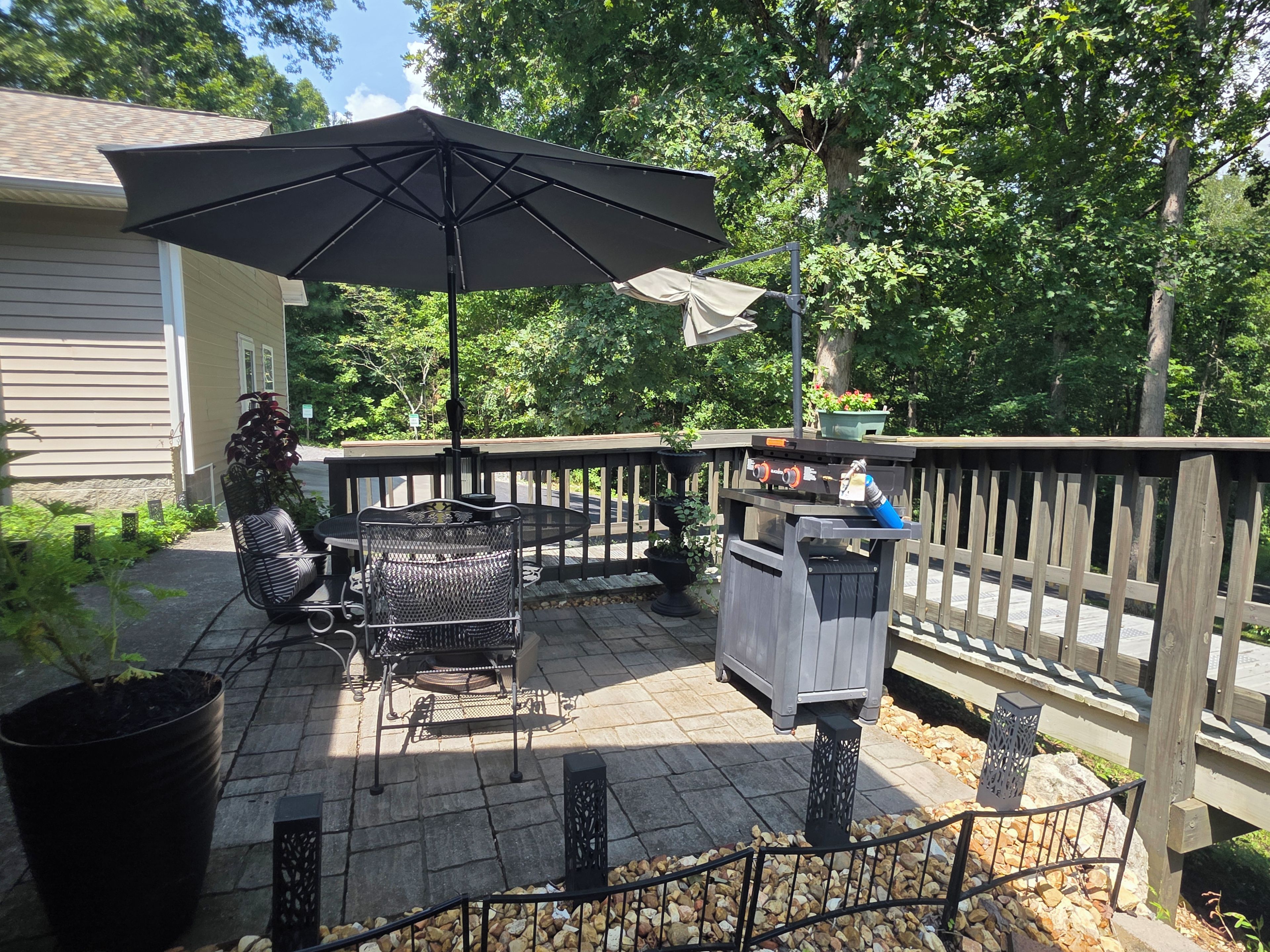 A patio with a table and chairs, a trash can, and a potted plant.