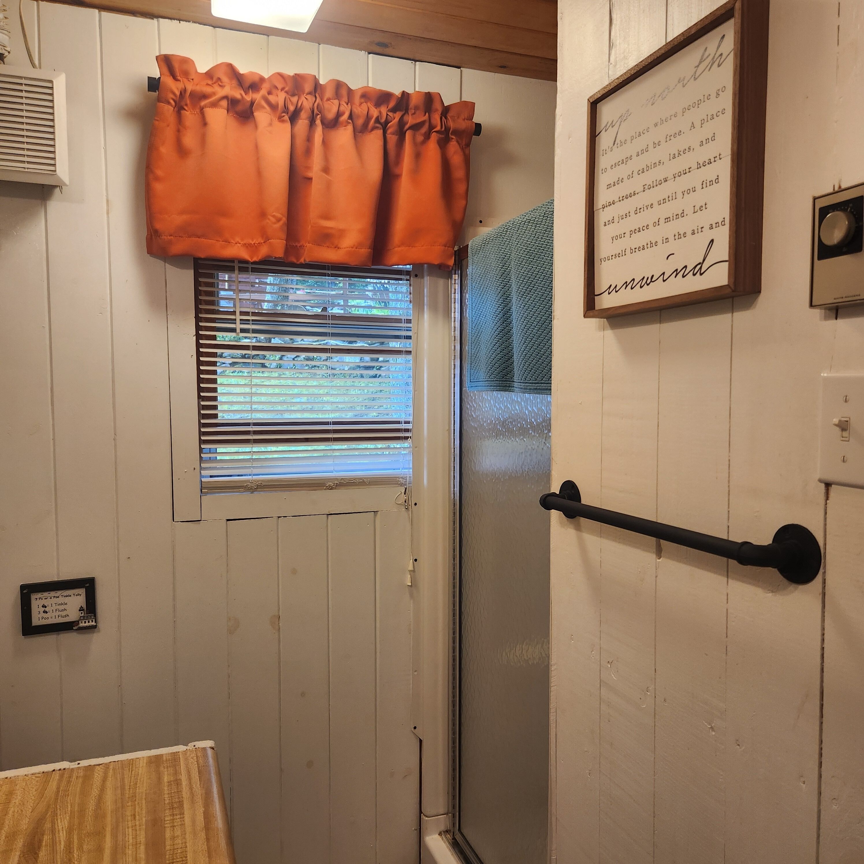 Une salle de bain avec une fenêtre, un porte-serviettes et une citation encadrée au mur.