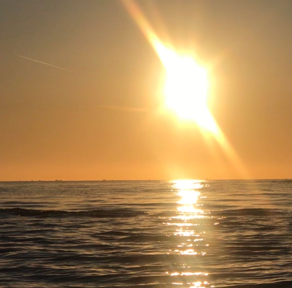 Een zonsondergang boven een rustige zee met een heldere horizon.