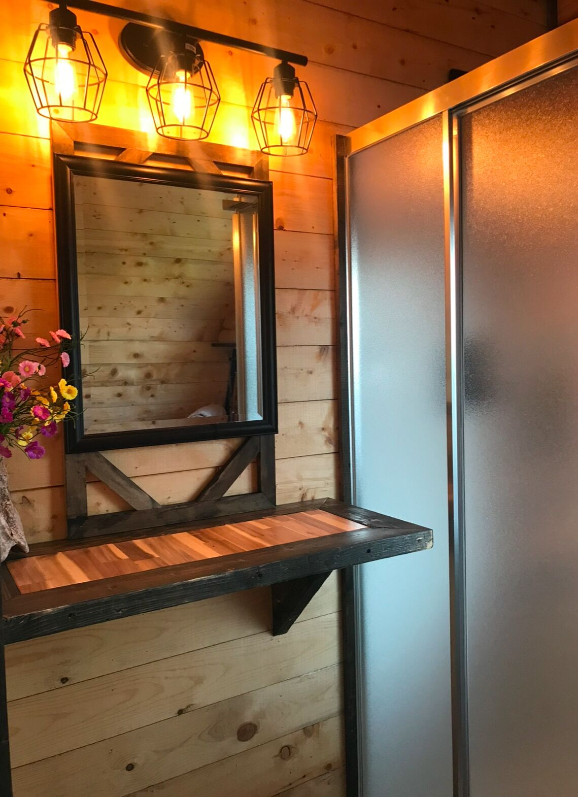 Een houten wand met een spiegel, een plank en een bloemstuk.
