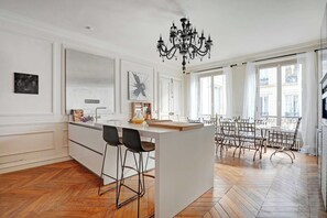 A spacious kitchen with a central island, bar stools, and a chandelier. - Charming Apartment - 4BR -10p- Madeleine (Paris)