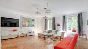 Un salón amplio con un televisor grande, un cuadro abstracto y colorido, un sofá rojo y un suelo de madera con diseño espiga.