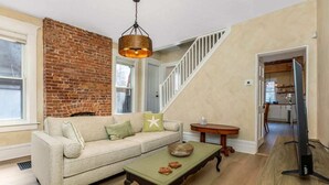 Un salon avec un mur en briques, un escalier, un canapé, une table basse et un téléviseur.